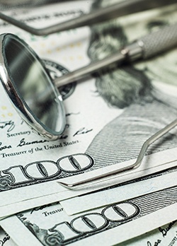 Dental tools laying on a stack of hundred-dollar bills